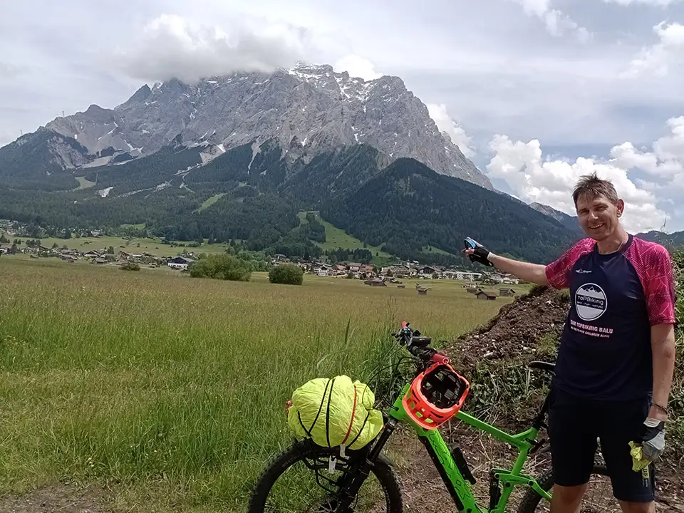 Christian Waniaus beim Alpencross, er deutet mit dem Finger auf einen großen Berg hinter sich